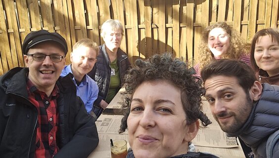 אַ גרופּע באַטייליקטע אין דער פּראָגראַם וואַרטן אויף אַ רומענישער מאָלצײַט אין אַן אָרטיקן רעסטאָראַן