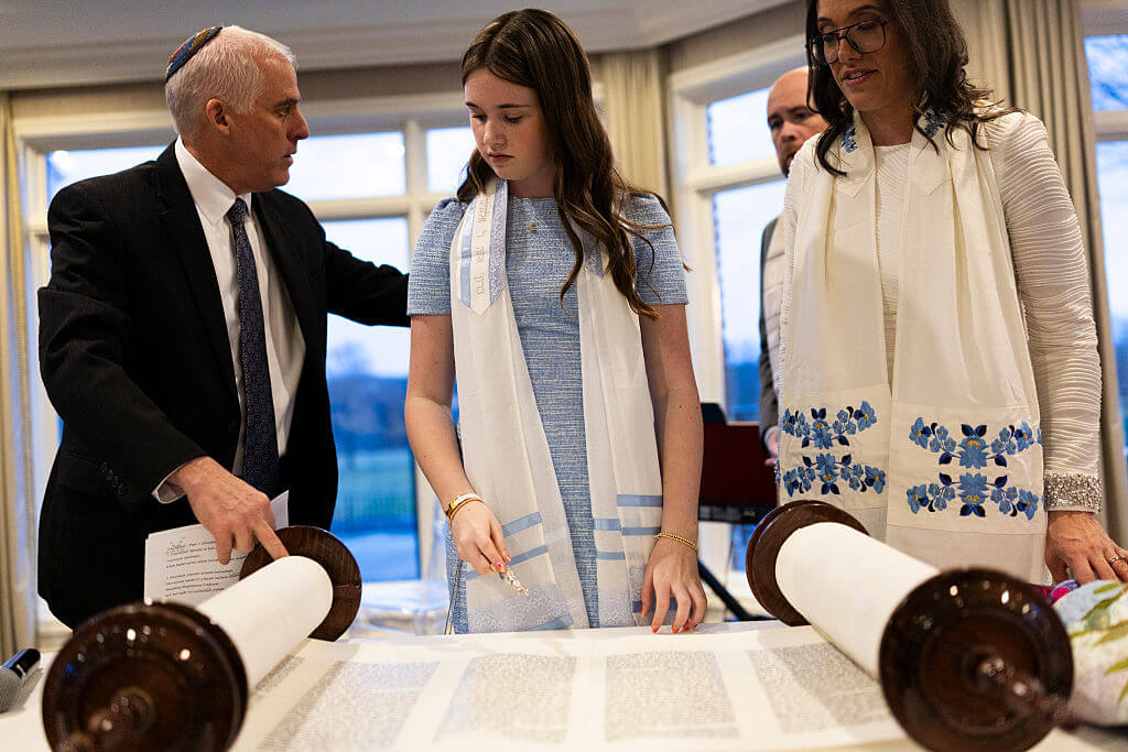 Rabbi Josh Bennett of Temple Israel speaks with Sydney Cox and her mother as they stand beside a Torah scroll ahead of Cox's bat mitzvah service at Tam O'Shanter Country Club on March 13 in West Bloomfield, Michigan. The ceremony was moved from Temple Israel after a gunman rammed a vehicle into the synagogue and opened fire.