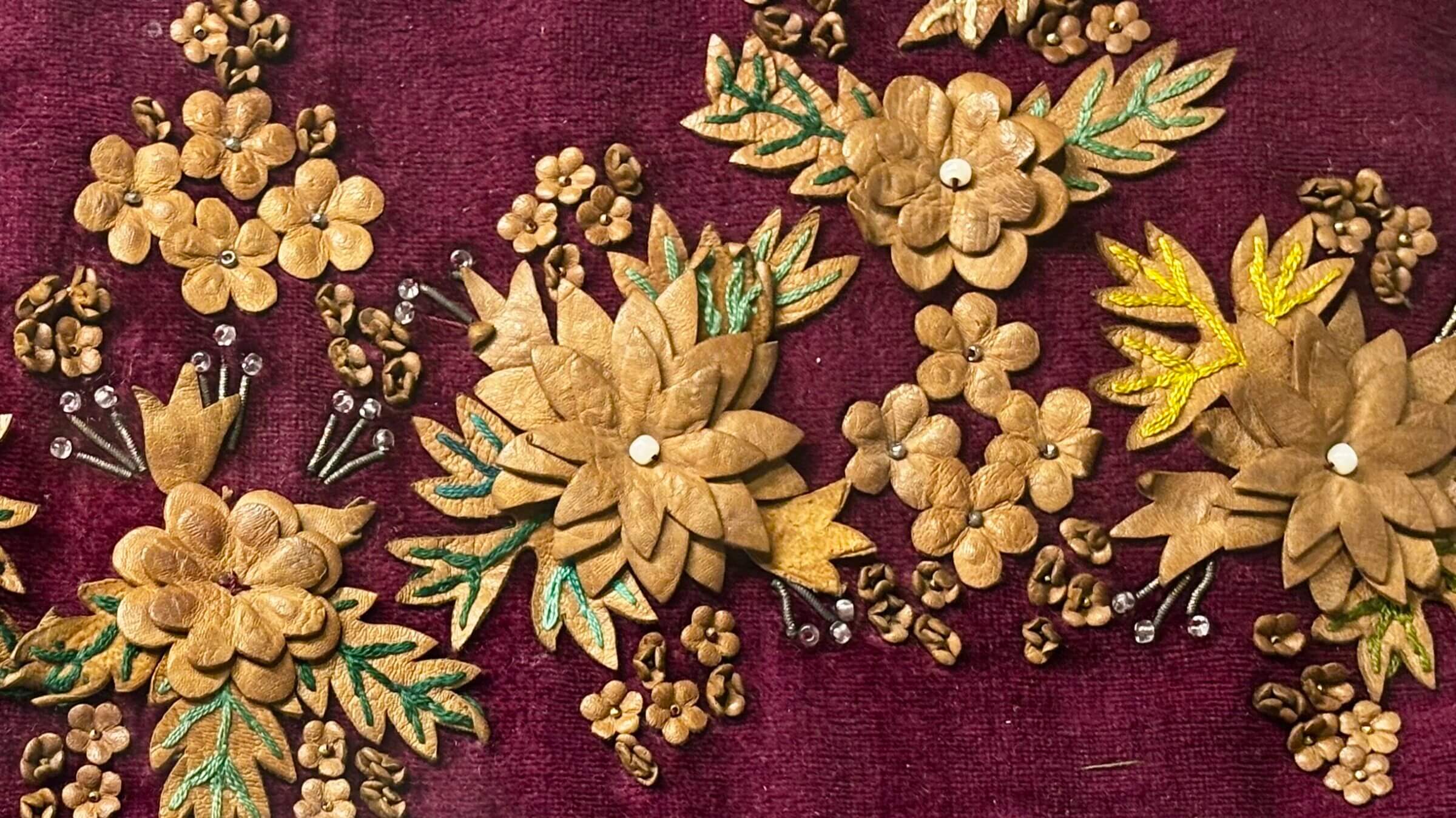 An intricately decorated 18th-century binder featuring intricate leatherwork flowers, embroidery and beads on plum-colored velvet.
