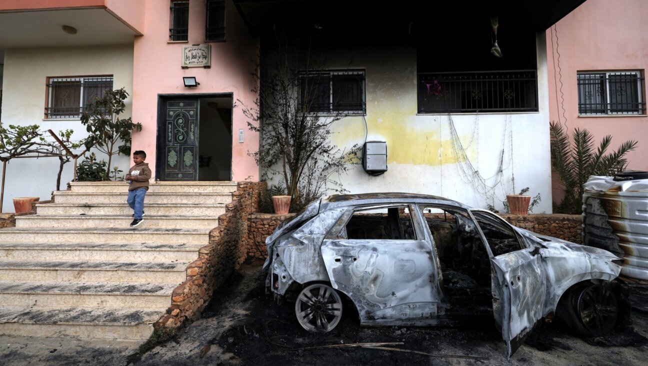 A Palestinian child stands outside a destroyed car and burnt out home following a reported attack by Israeli settlers in the village of Deir al-Hatab, east of the city of Nablus, in the Israeli-occupied West Bank on March 23, 2026. (JAAFAR ASHTIYEH / AFP)