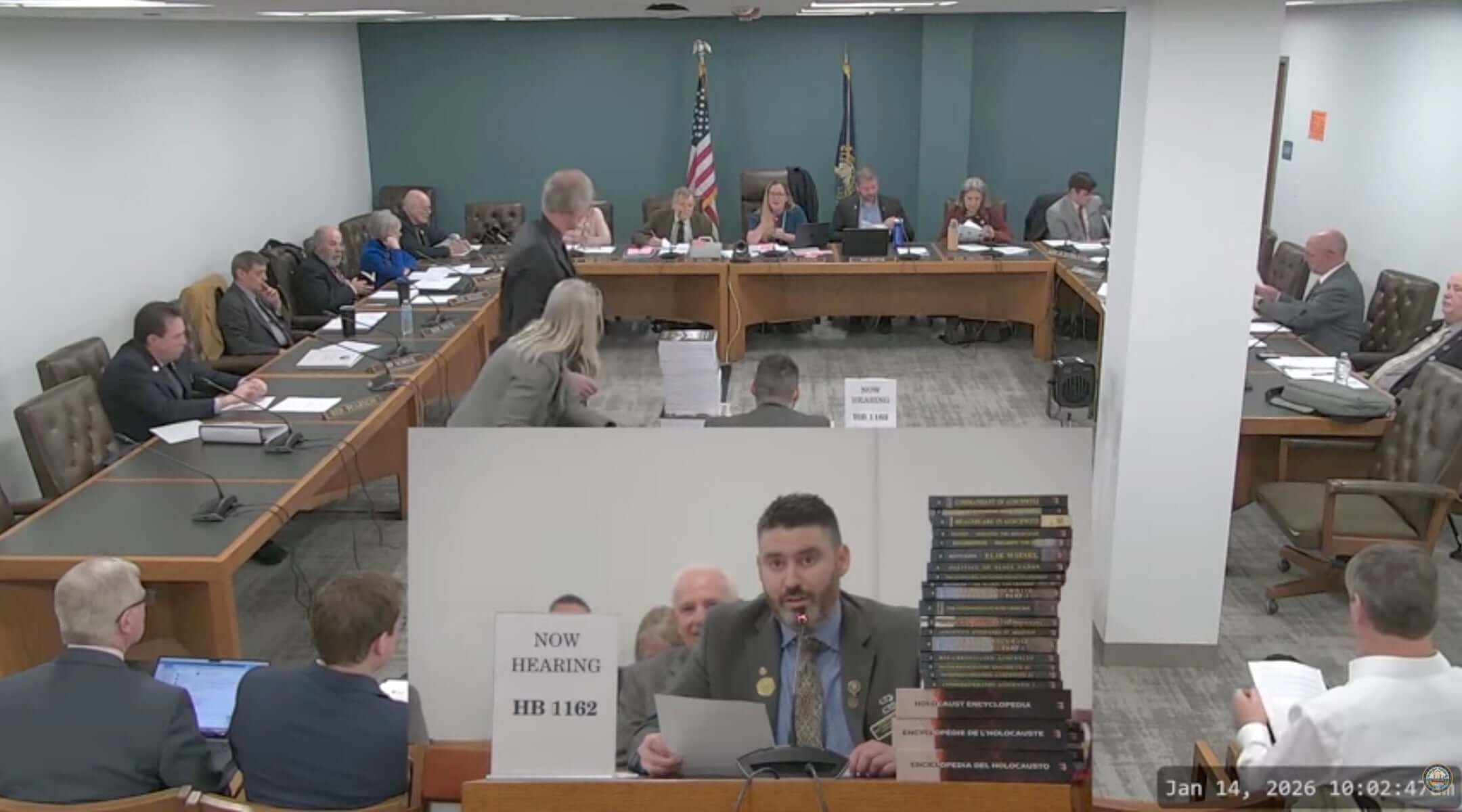 New Hampshire GOP state Rep. Matt Sabourin dit Choinière (center) testifies before a state committee on his proposed amendment to add a Holocaust denier to the state’s Holocaust education commission, Jan. 14, 2026. He is flanked by a stack of Holocaust-denial books. (Screenshot)