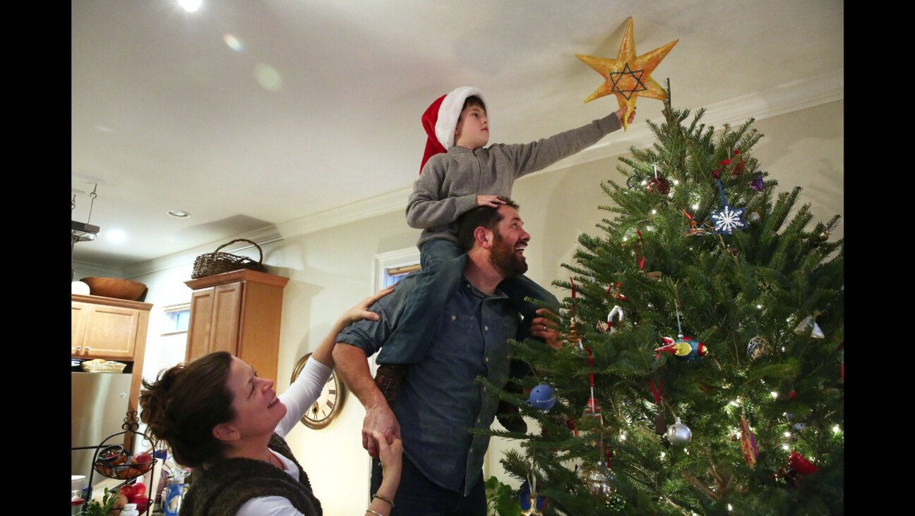 Karolyn Feeks Maws, who is Christian, her Jewish husband, Tony Maws, and their 8-year-old son Charlie Maws, decorate their Christmas tree with a homemade Star of David. (Pat Greenhouse/The Boston Globe via Getty Images)