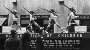People view an anti-Nazi display with statues of young boys wearing shorts, armbands, gas masks and carrying rifles, Rockefeller Center, New York City. 