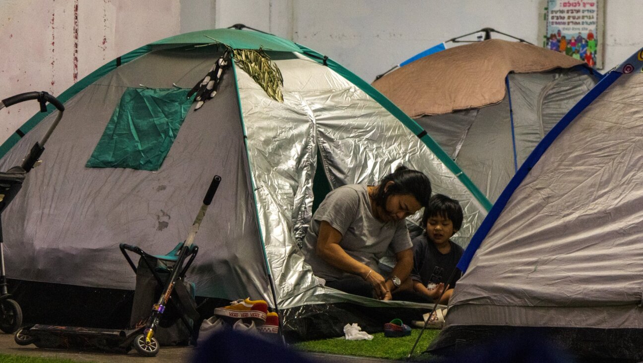 A mother and child sit at the entrance to a tent in the shelter. (Theia Chatelle)