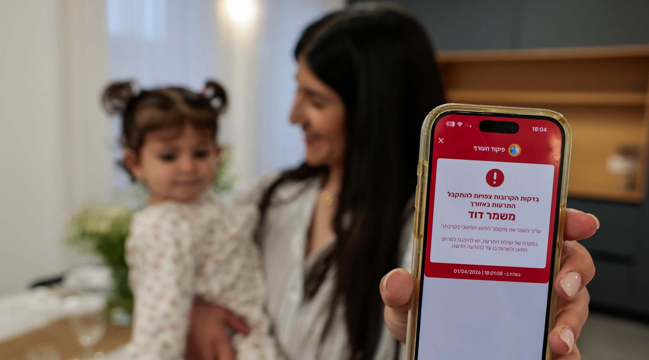 A woman shows a missile alert notification on her mobile phone as residents take cover indoors following missile fire from Iran toward Israel on the eve of the Passover, in Mishmar David, April 1. 2026.