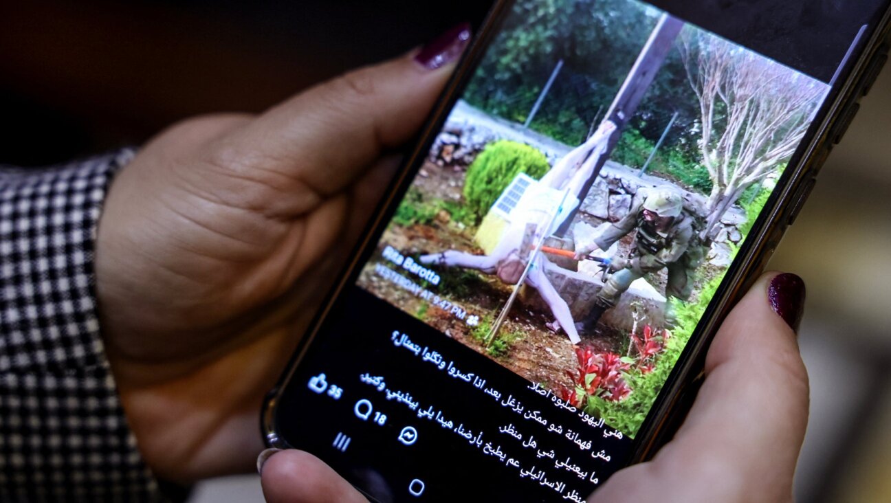 A woman checks a social media post on her mobile phone featuring an image that appears to show an Israeli soldier hitting a statue of Jesus Christ in the southern Lebanese Christian village of Debl, in Beirut on April 20, 2026. (Anwar AMRO / AFP)