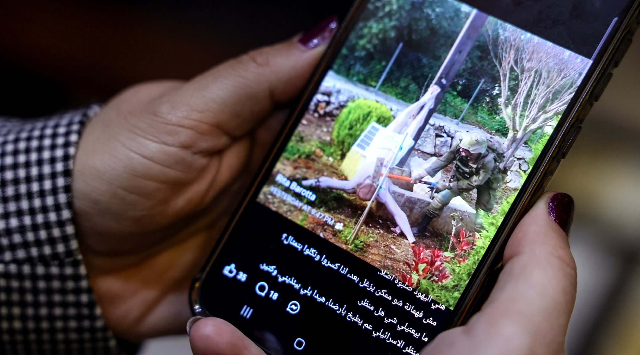 A woman checks a social media post on her mobile phone featuring an image that appears to show an Israeli soldier hitting a statue of Jesus Christ in the southern Lebanese Christian village of Debl, in Beirut on April 20, 2026. (Anwar AMRO / AFP)