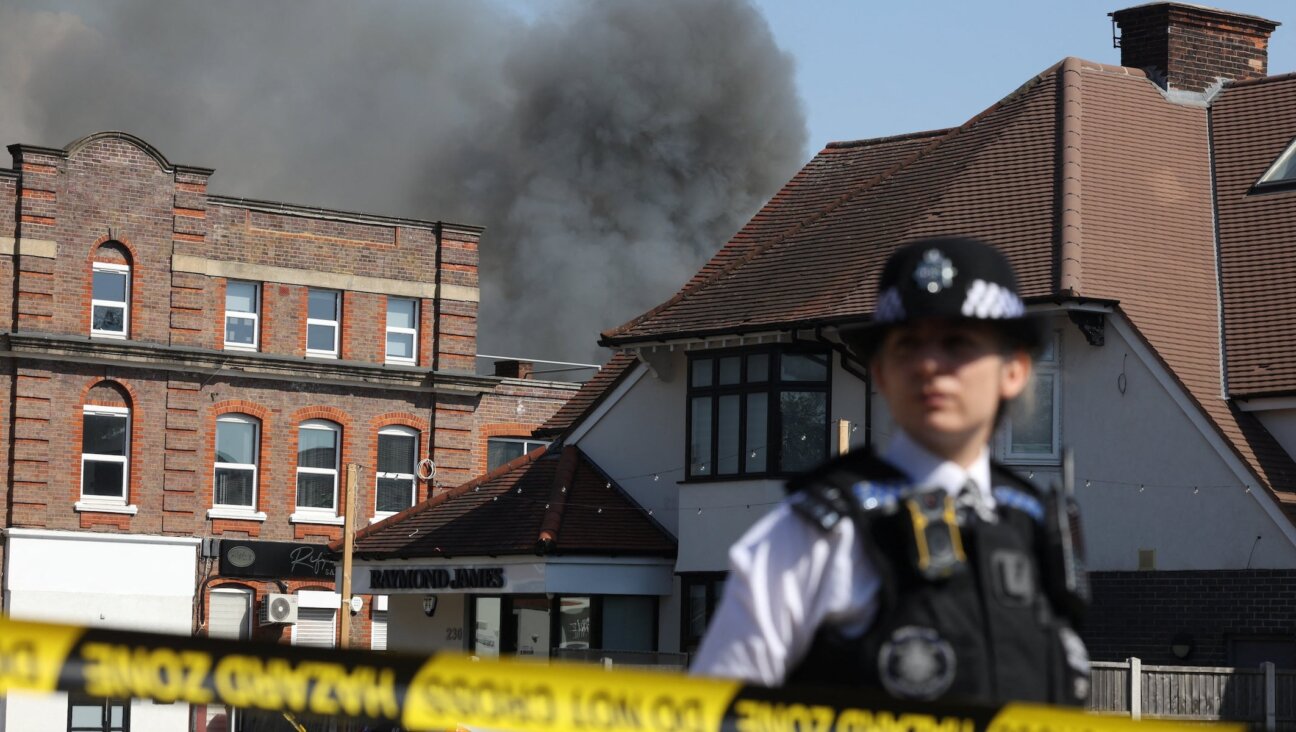 A member of the police stands at a cordoned area as smoke rises in the background from a fire that broke out at a kosher supermarket in the Golders Green neighbourhood in north London, May 27, 2026.