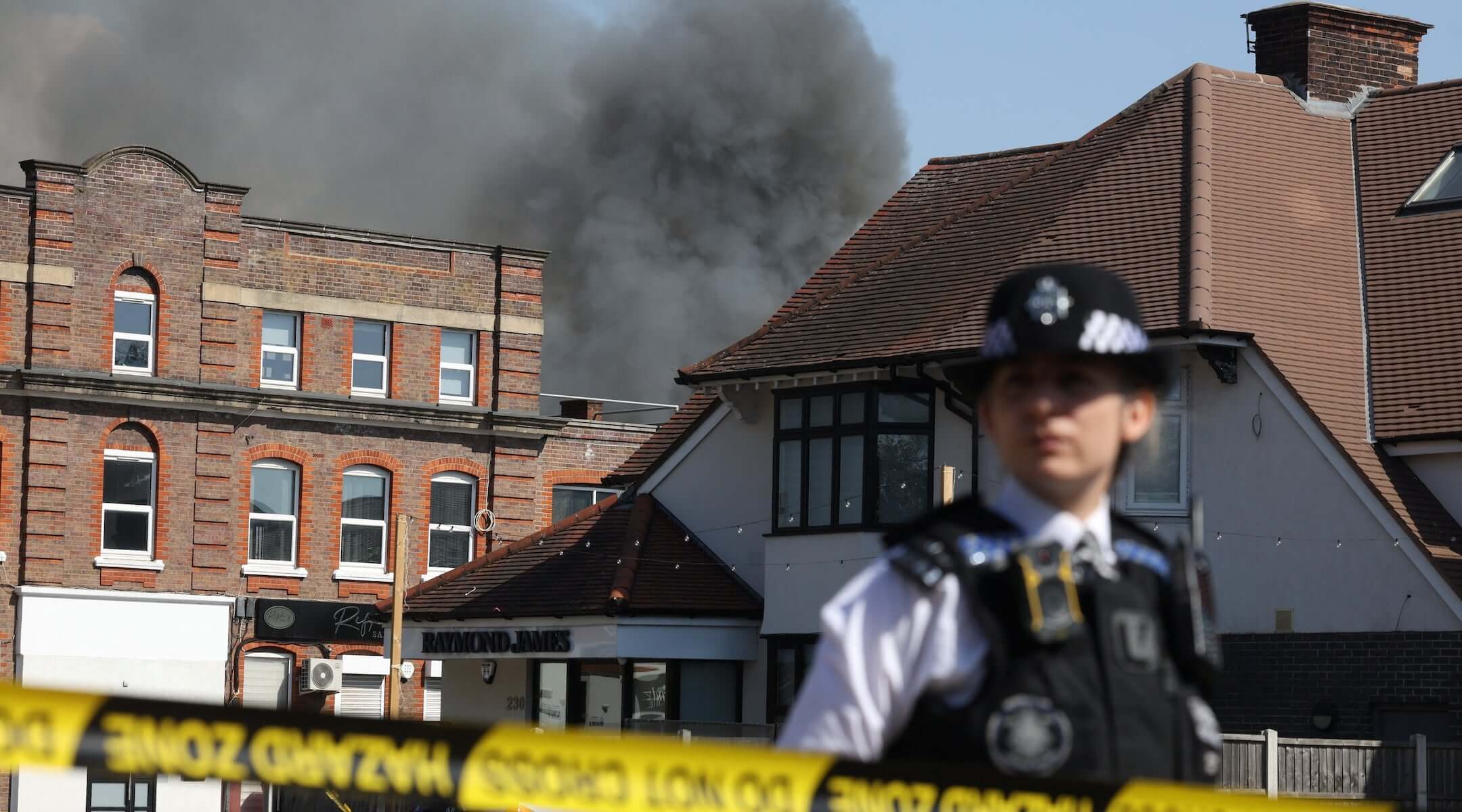A member of the police stands at a cordoned area as smoke rises in the background from a fire that broke out at a kosher supermarket in the Golders Green neighbourhood in north London, May 27, 2026.