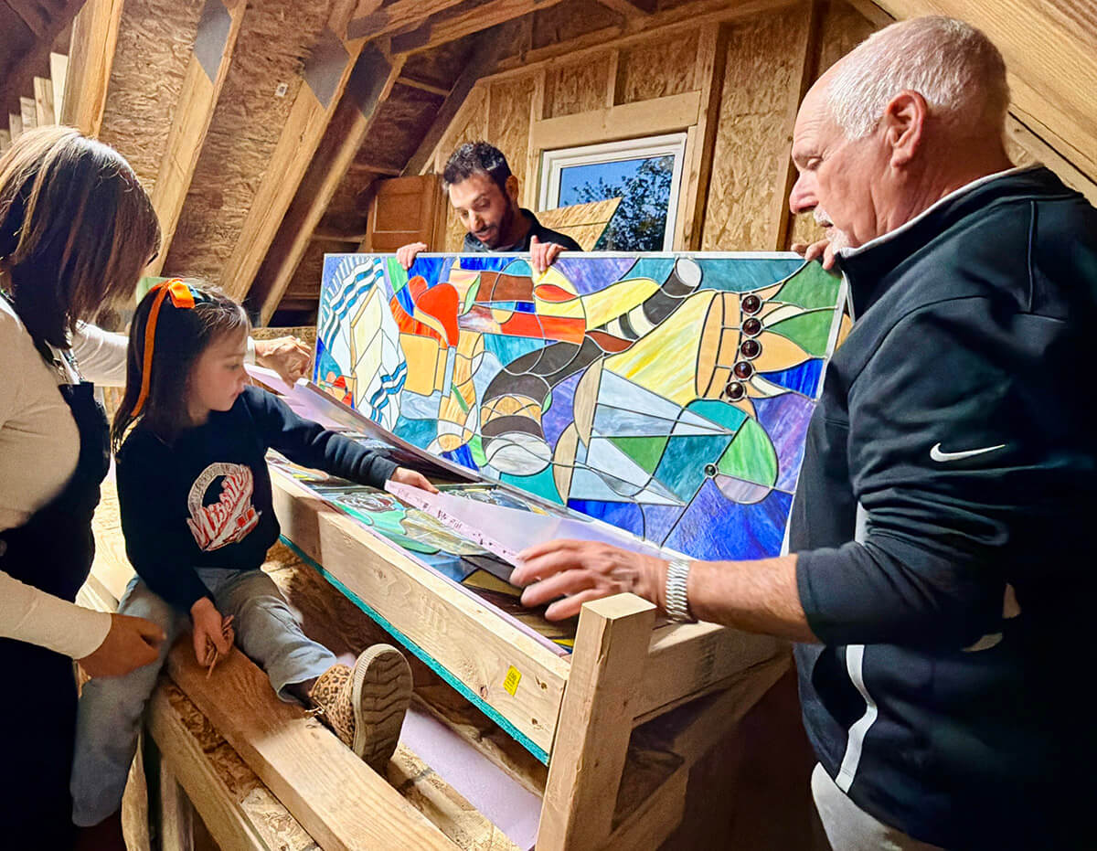 Left to right: Margo Jakobs shows the stained glass to her granddaughter, Annie, while Nik Jakobs and his dad, Dave Jakobs watch.